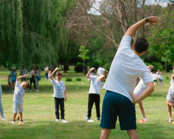 Children and instructors stretching in a park during a summer physical education class.