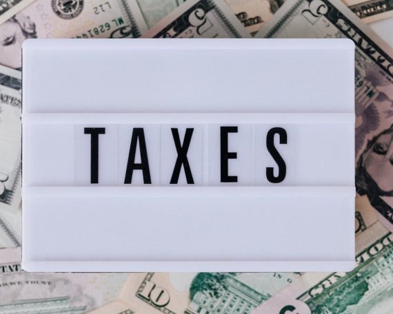 Top view of white vintage light box with TAXES inscription placed on stack of USA dollar bills on white surface